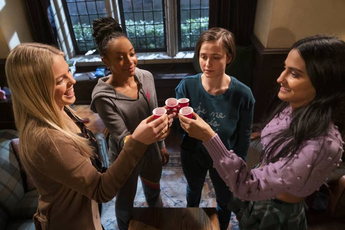 Four female college freshmen &quot;cheers&quot; with shot glasses. Three are happy. One in the middle looks apprehensive.