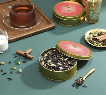 Close-up of one of the opened gold tins of chai surrounded by tea accessories