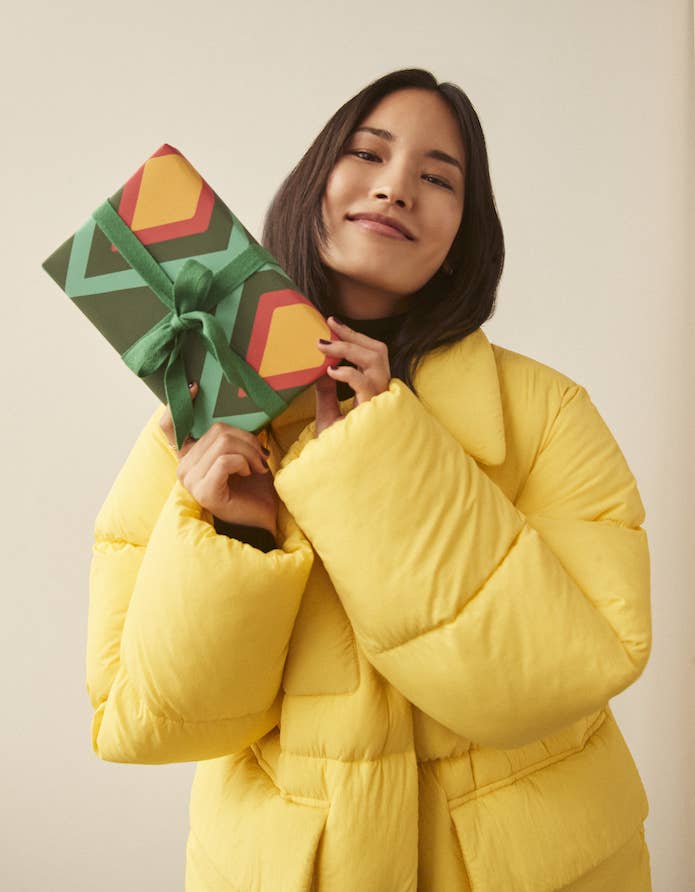 woman in yellow jacket holding up a wrapped gift