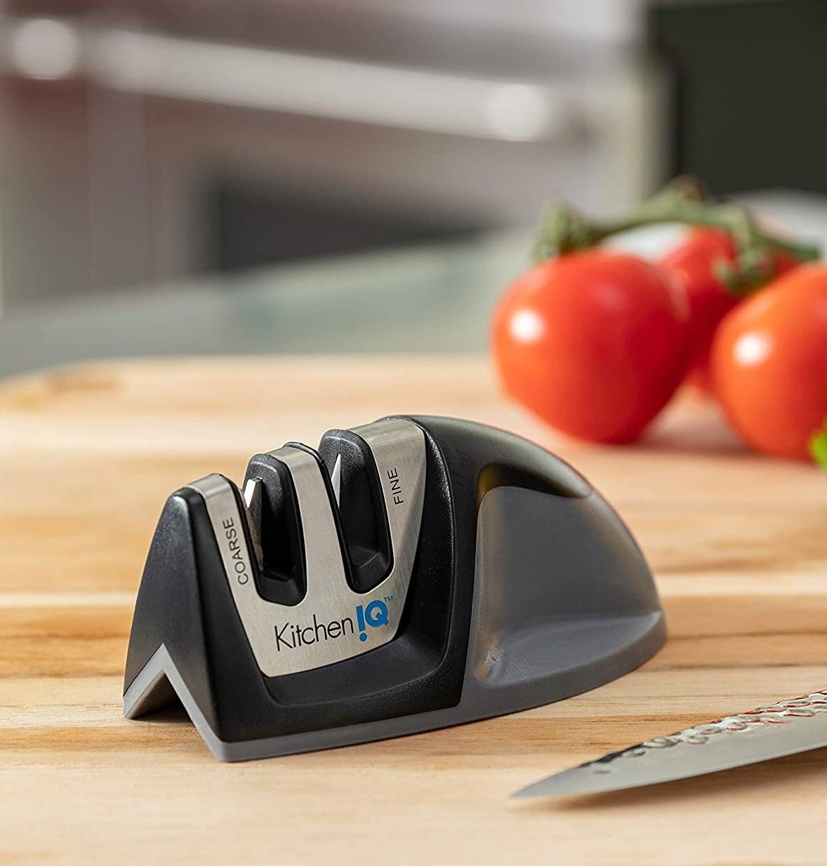The knife sharpener on a wood cutting board next to a knife and some tomatoes