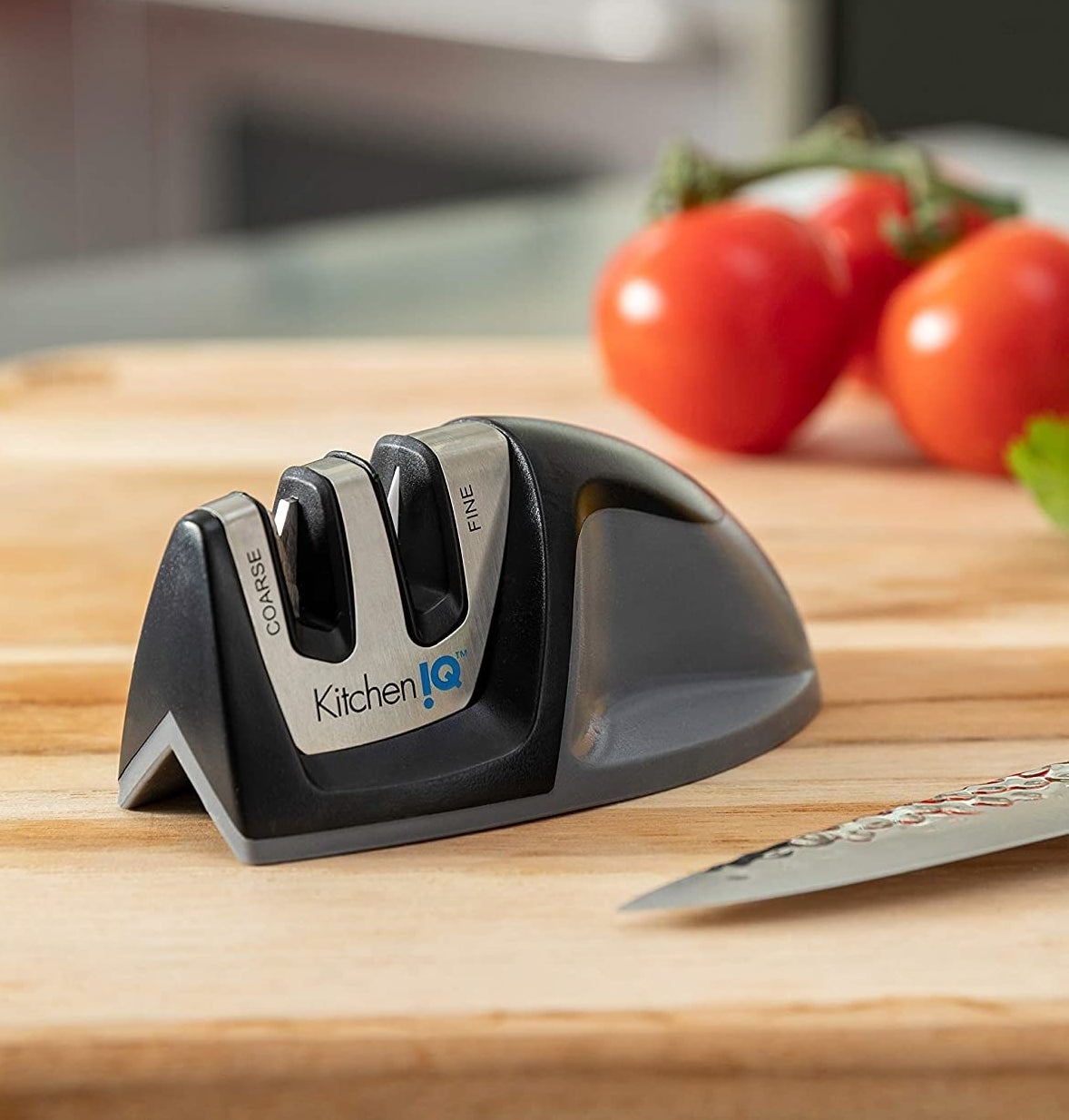 The knife sharpener on a wood cutting board next to a knife and some tomatoes