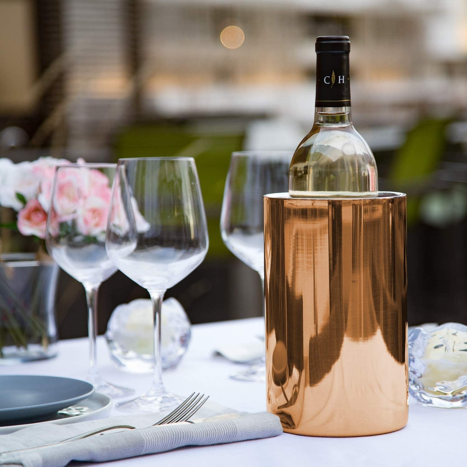 The copper chilling bucket holding a bottle of wine on top of a set table