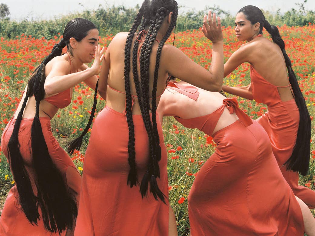 Four women in dresses with long hair dancing in a field of flowers