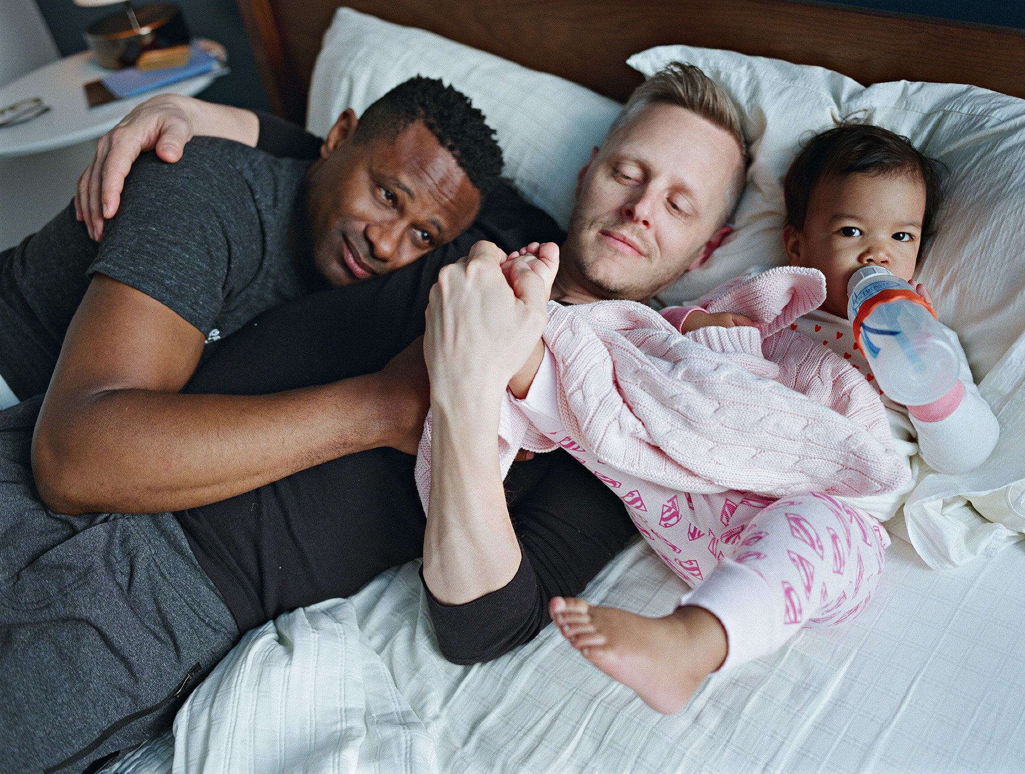 A gay couple with a baby all lying on the bed