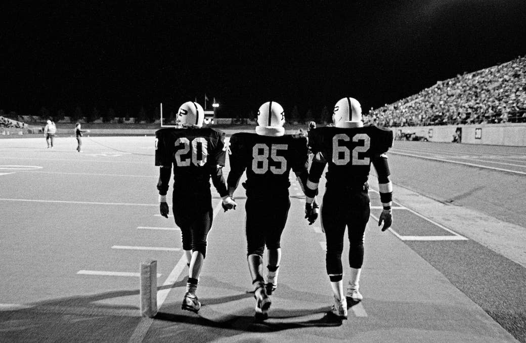 Three football players holding hands and walking onto the field