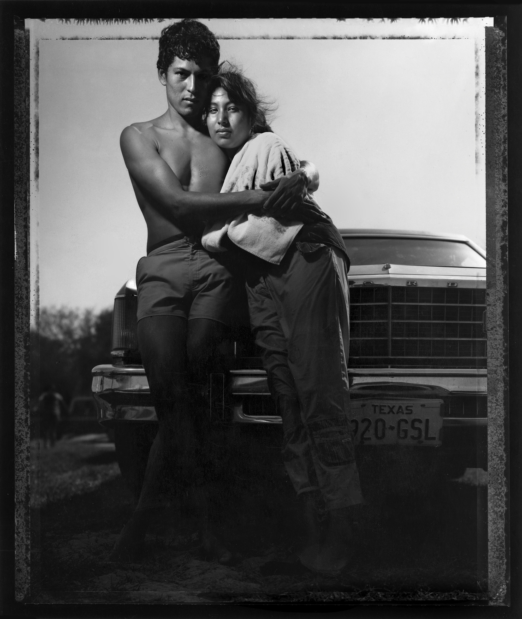 A young couple embracing in front of a car outside