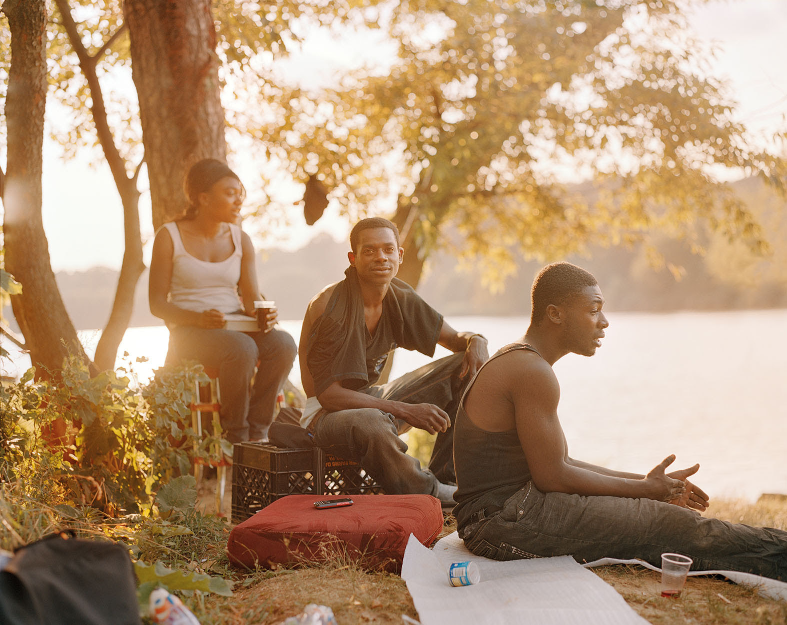 Three people sitting outside in a park at sunset with a picnic