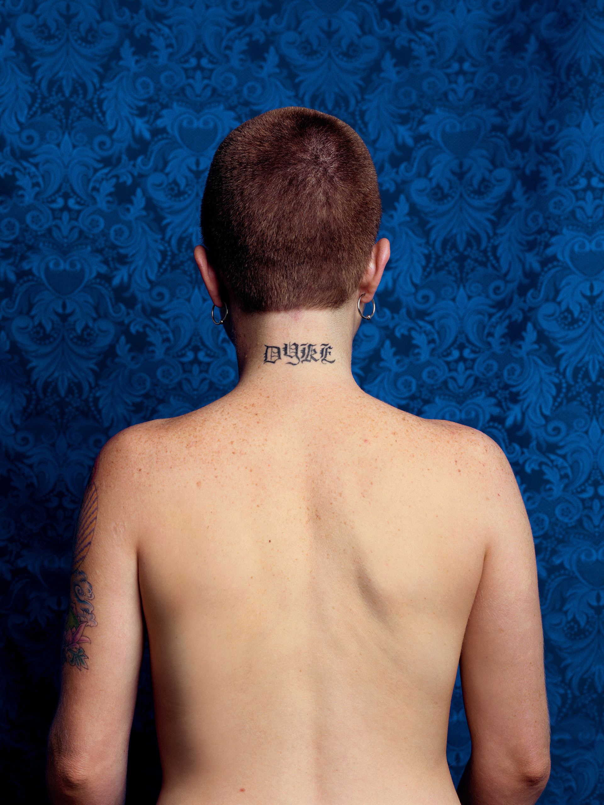 The bare back of a woman with the word dyke tattooed on her neck