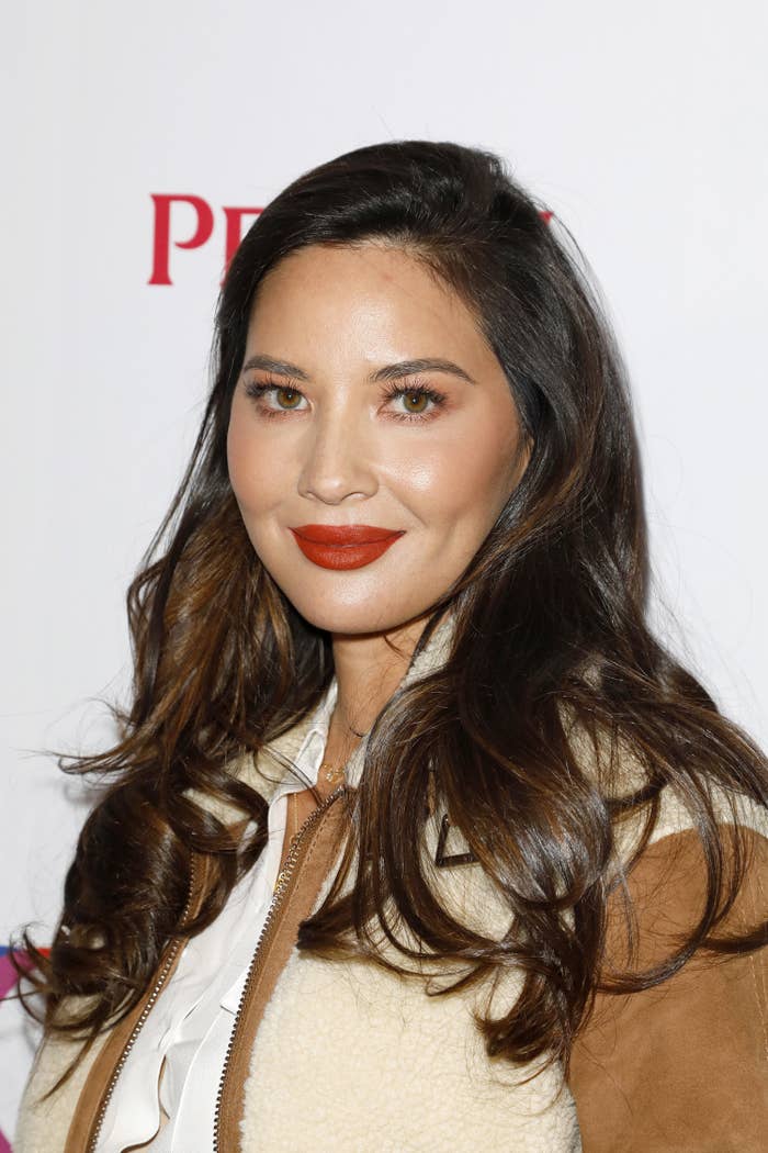 Olivia Munn smiles for the camera while wearing a jacket and blouse