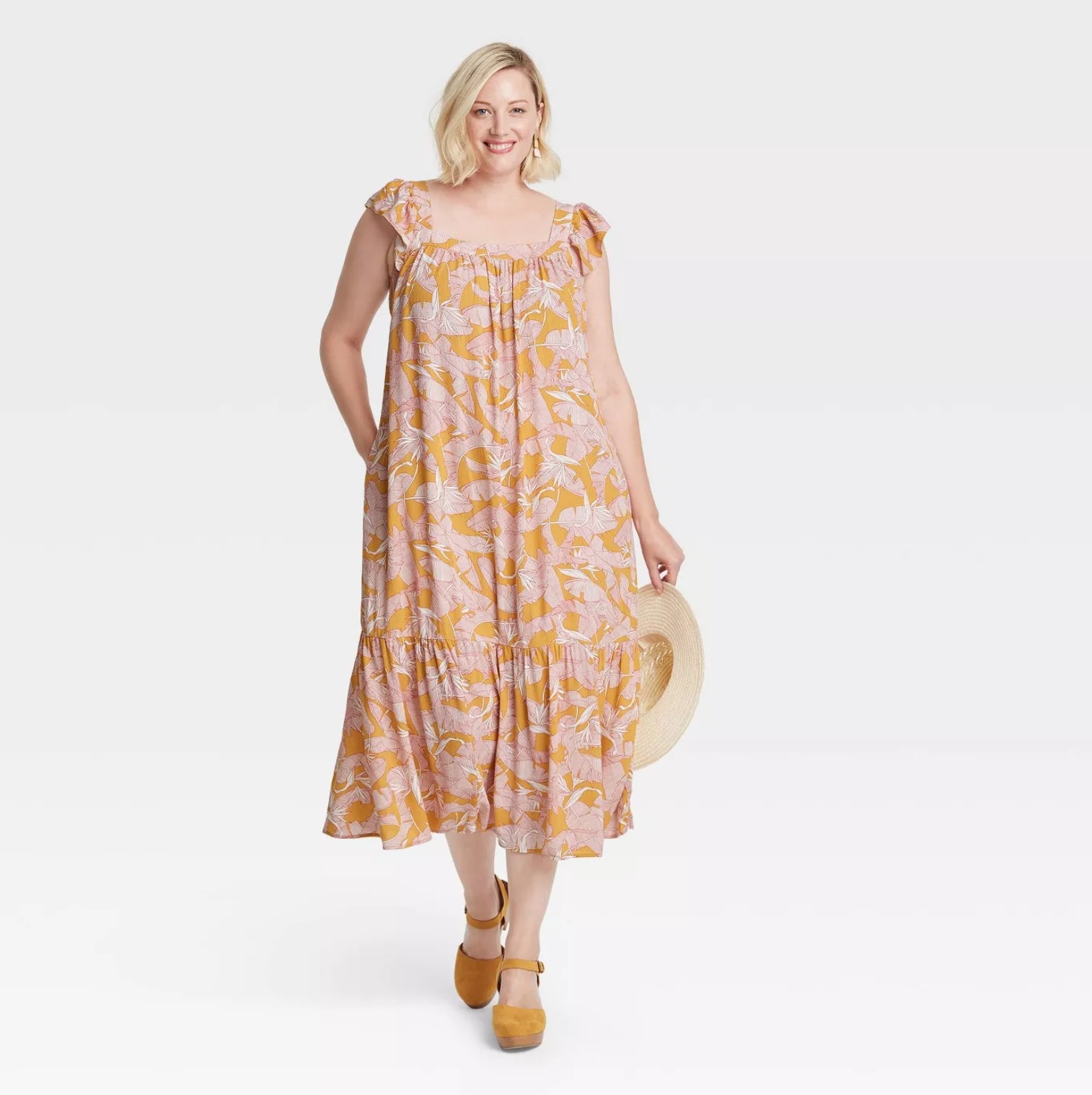 Model wearing the pink and orange patterned dress carrying a sunhat and wearing mustard shoes