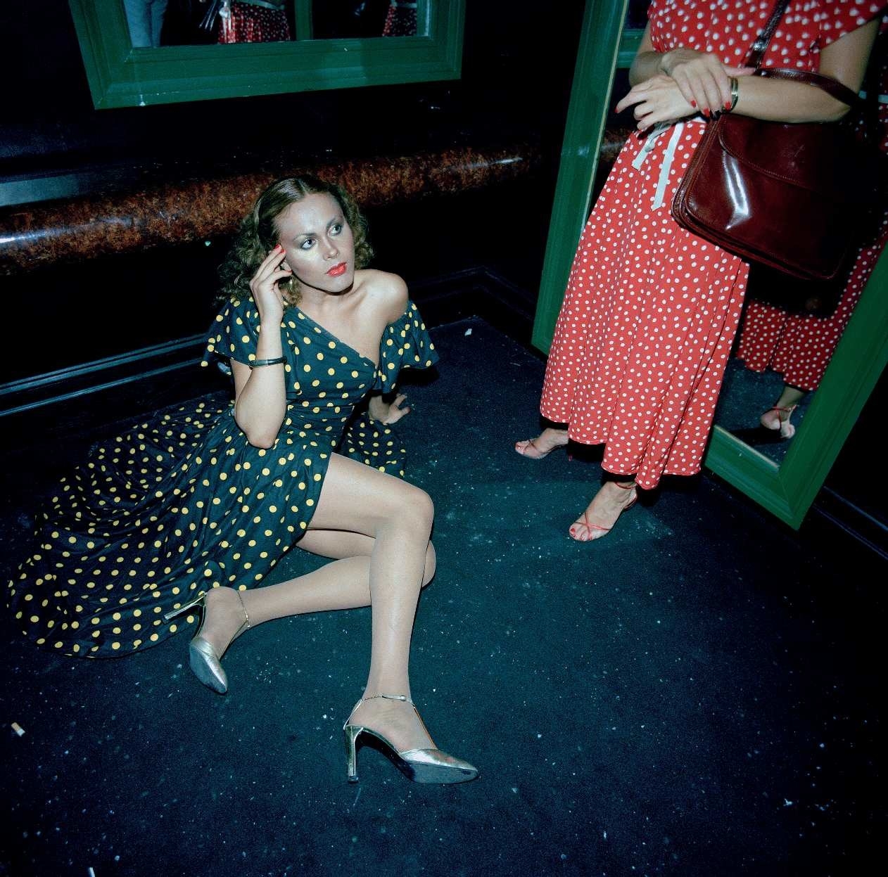 A woman in a dress sitting on the ground while another woman stands next to her