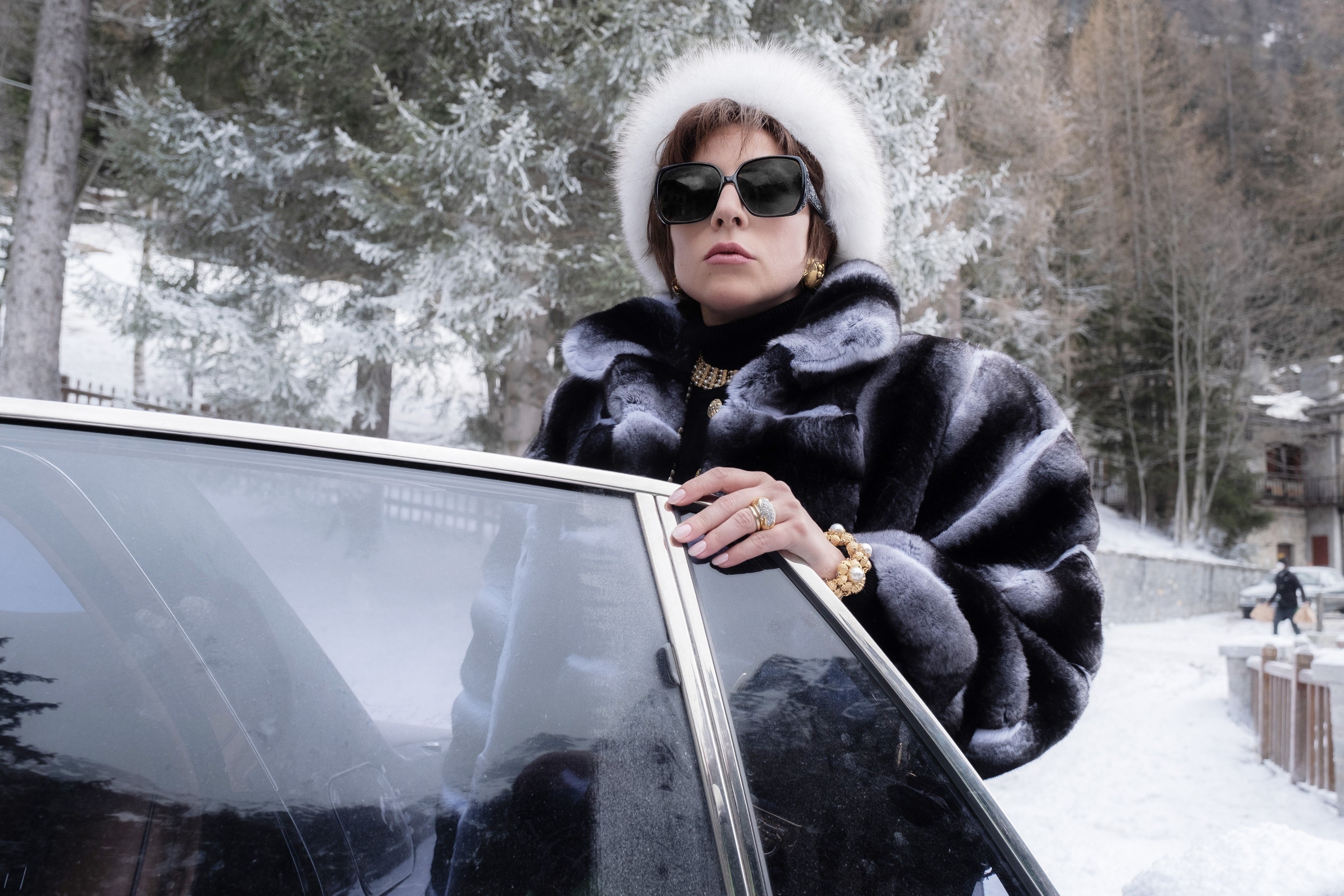 Gaga as Patrizia in a fur coat standing next to a car in a snowy setting
