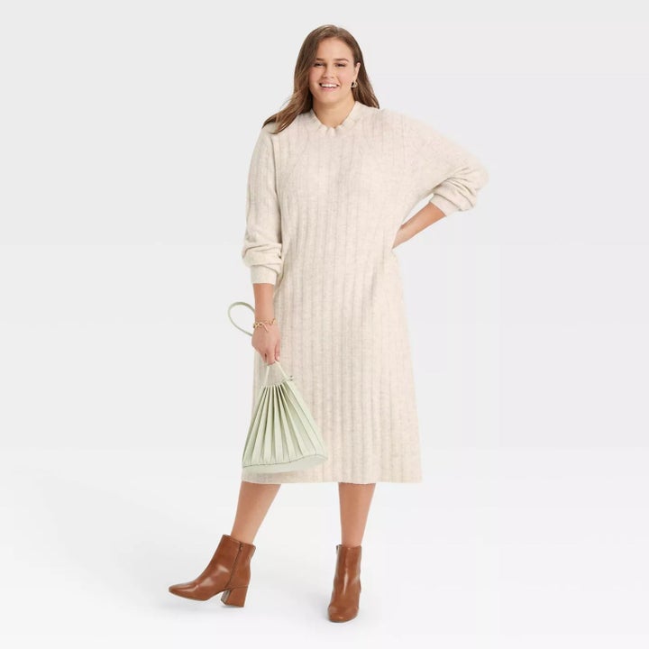 model wearing the sweater dress in cream with brown booties carrying a mint handbag