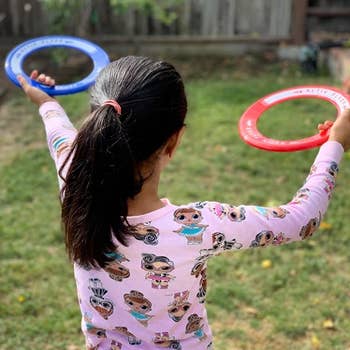 reviewer's photo showing their child holding the red and blue flying rings in the yard