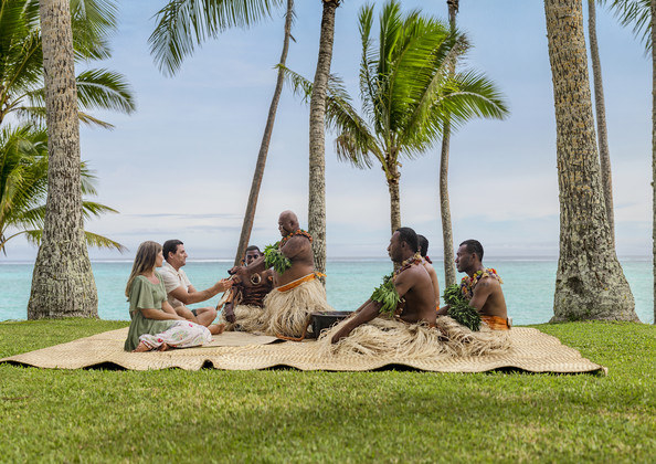 Two tourists sitting with native Fijian people, learning about the culture and traditions