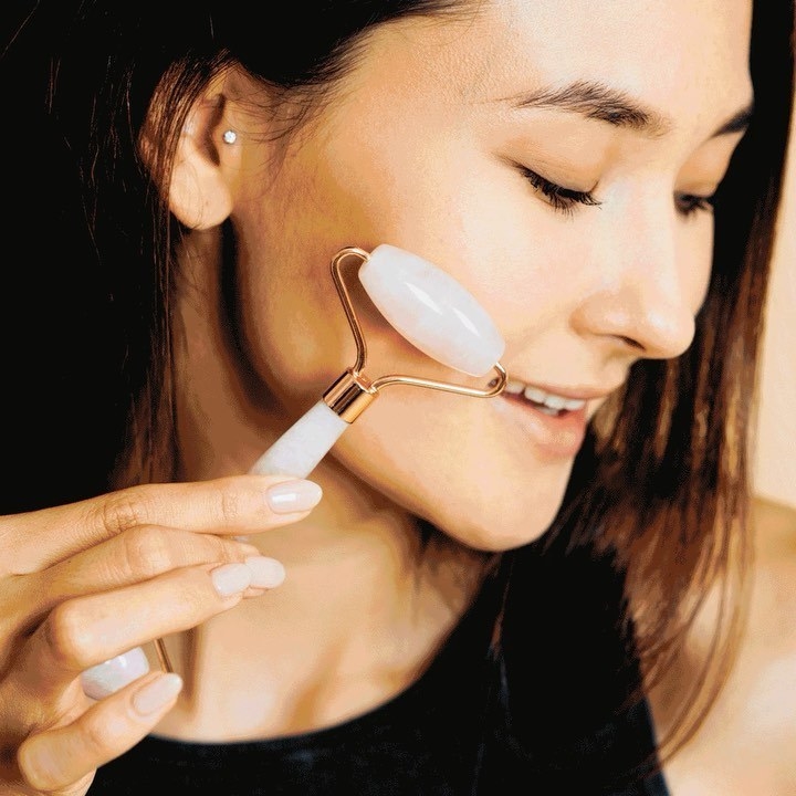a smiling person using the facial roller on their cheek