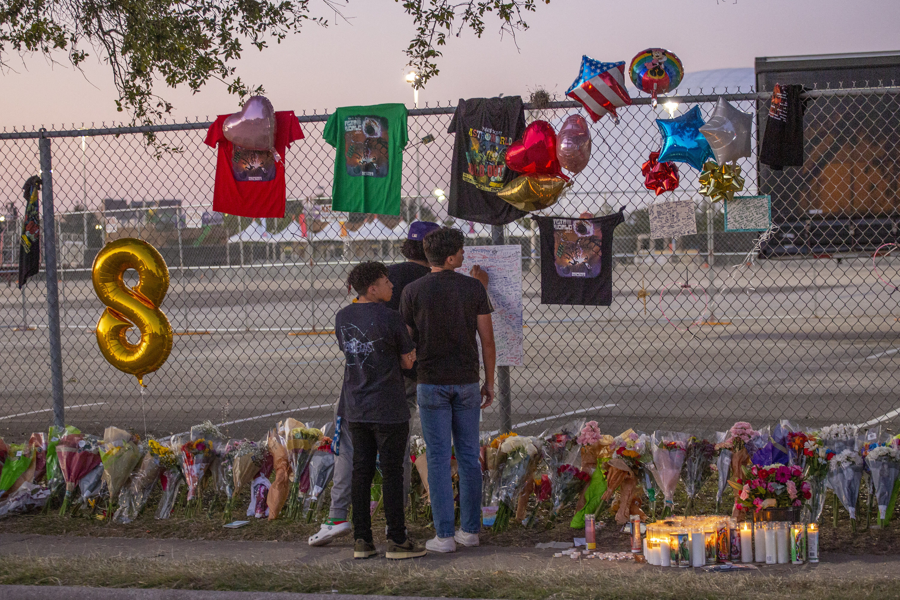 High school friends who attended the Travis Scott concert, Isaac Hernandez and Matthias Coronel, watch Jesus Martinez sign a remembrance board at a makeshift memorial on Nov. 7, 2021, at the NRG Park grounds