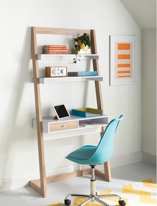 White and light brown desk with bright blue chair and office supplies and books on desk