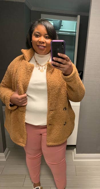 reviewer in light tan teddy jacket, a white turtleneck, and pink pants