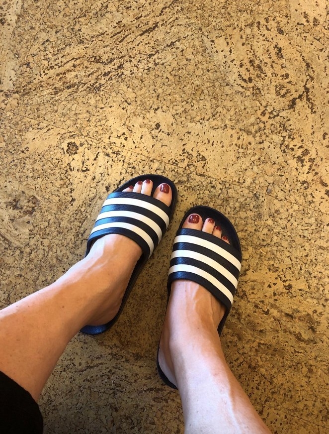 Reviewer wearing black adidas slides with white stripes on front