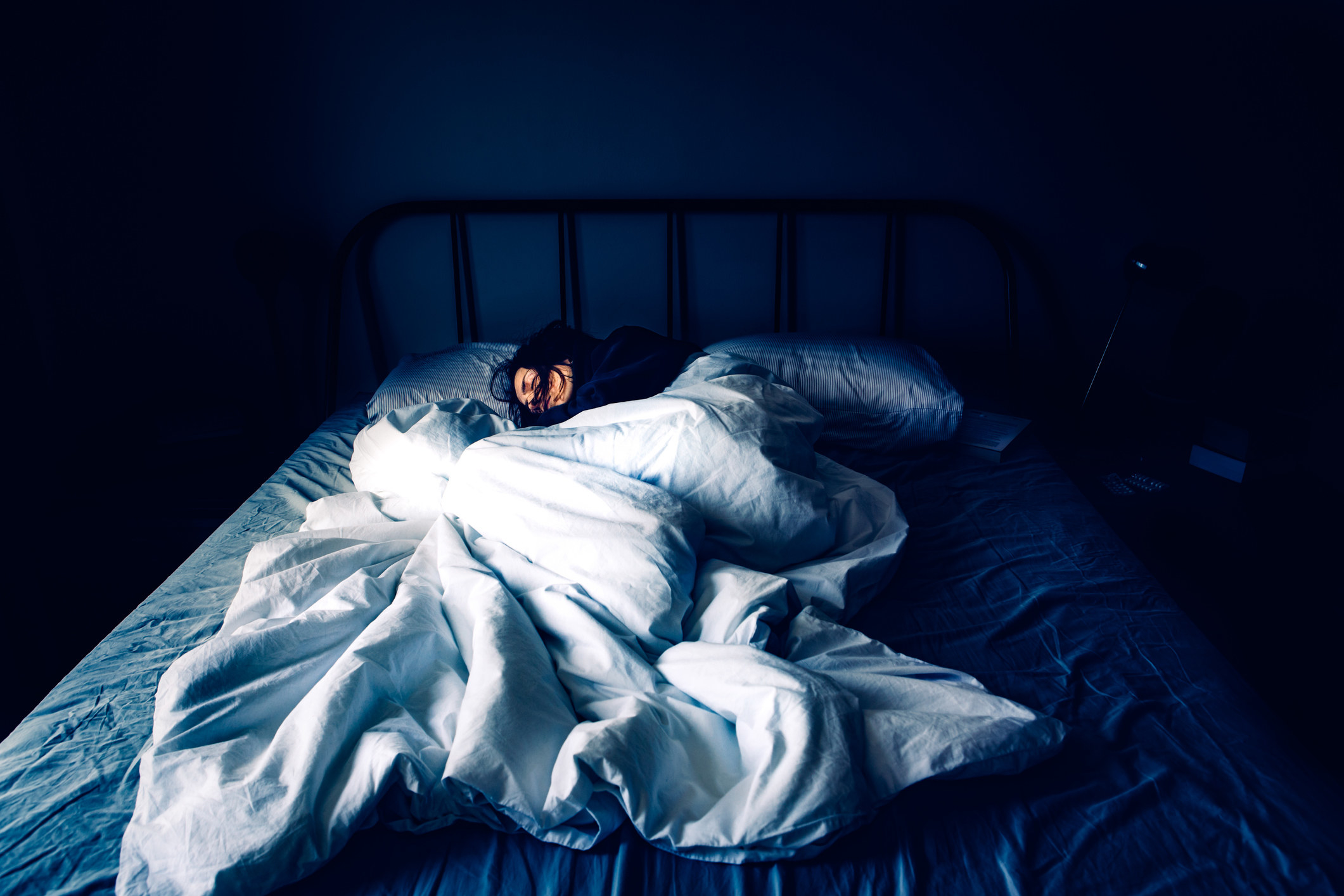 A person sleeps in bed under a large comforter