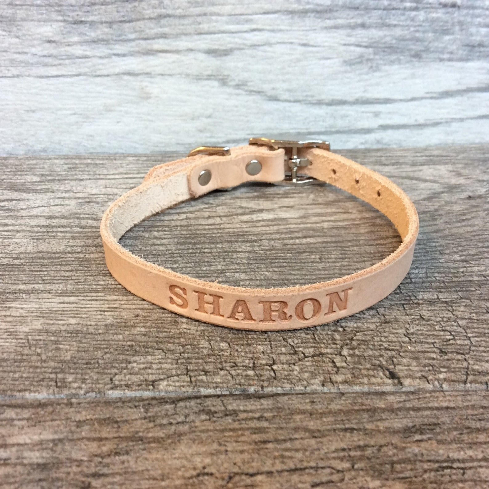 An off white cat collar with a name engraved on it.
