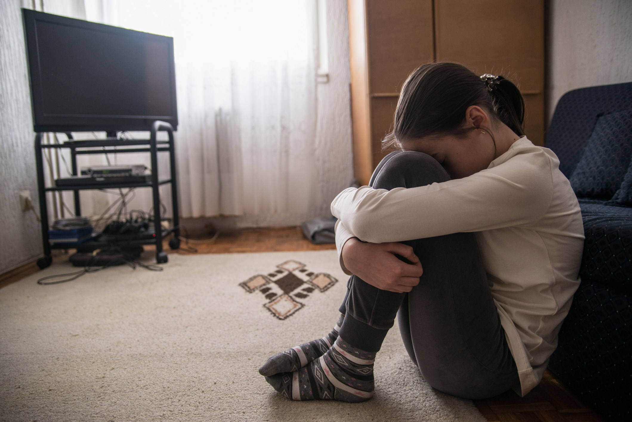 A girl clutches her knees with her head against her thighs while crying