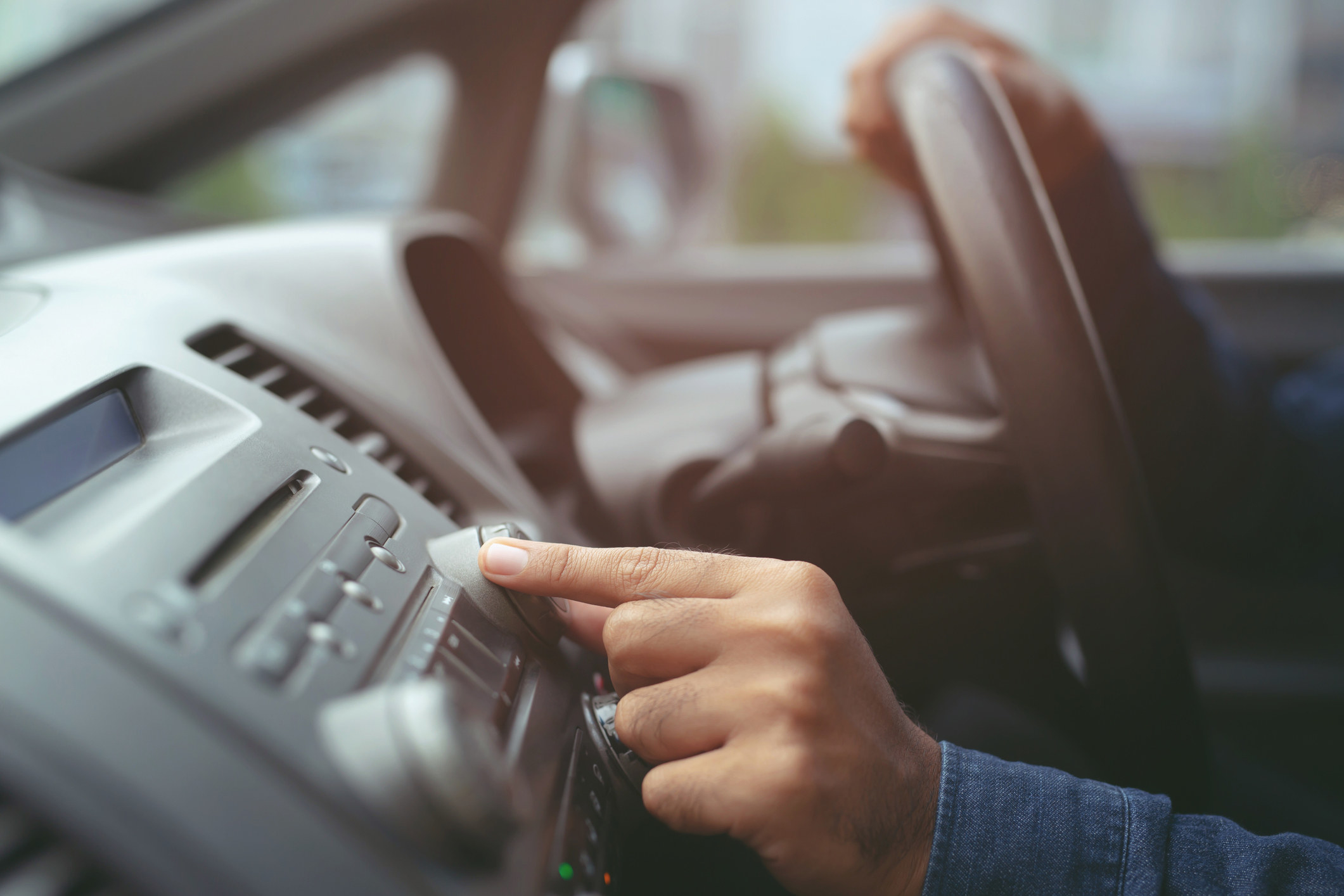 A hand turns the volume knob on a car radio