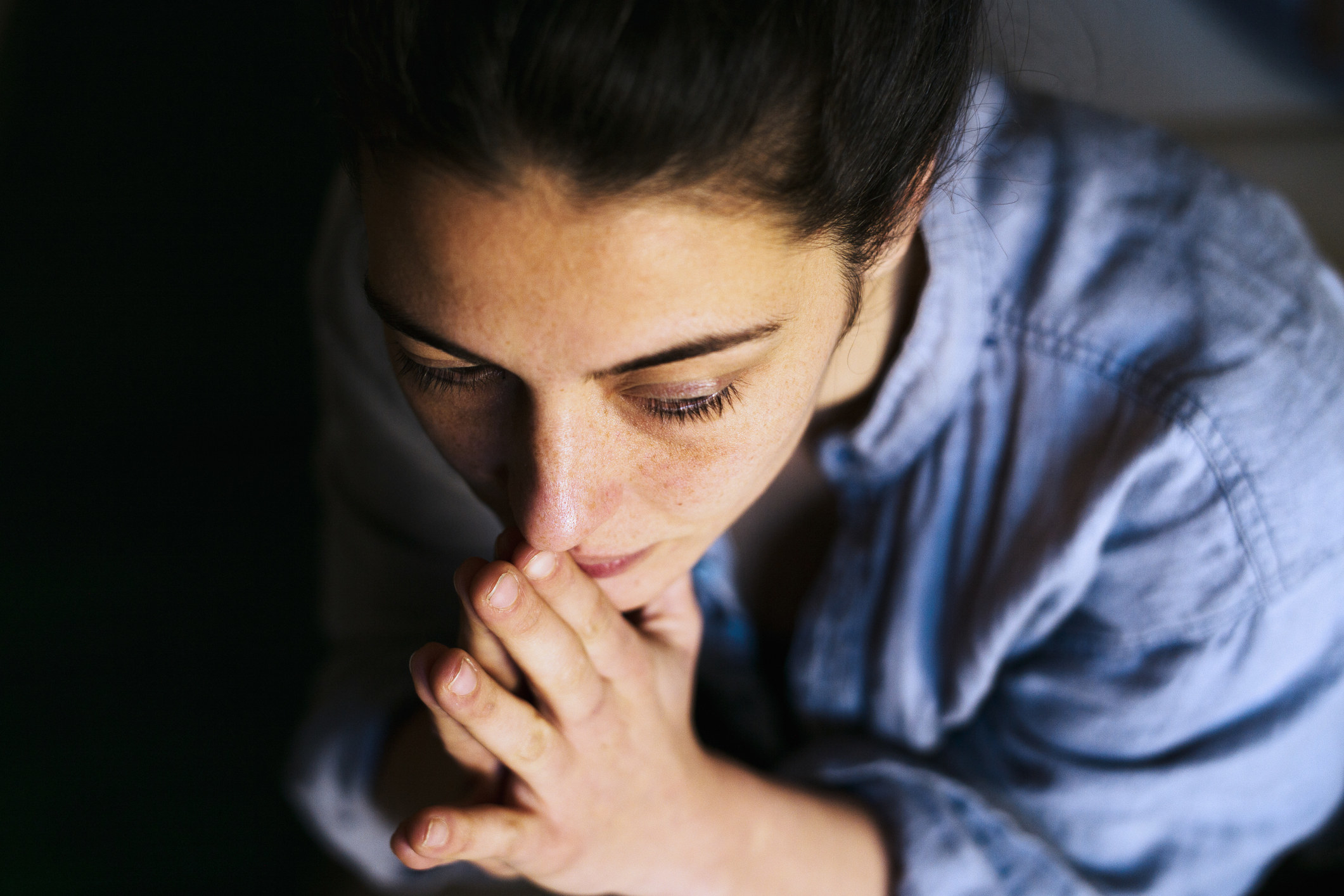 A concerned woman sits with her hands clasped in prayer