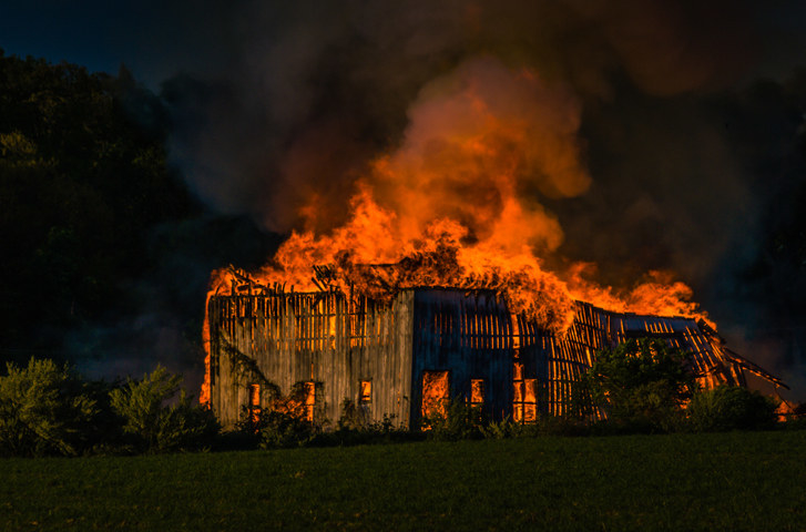A barn burns in flames at night