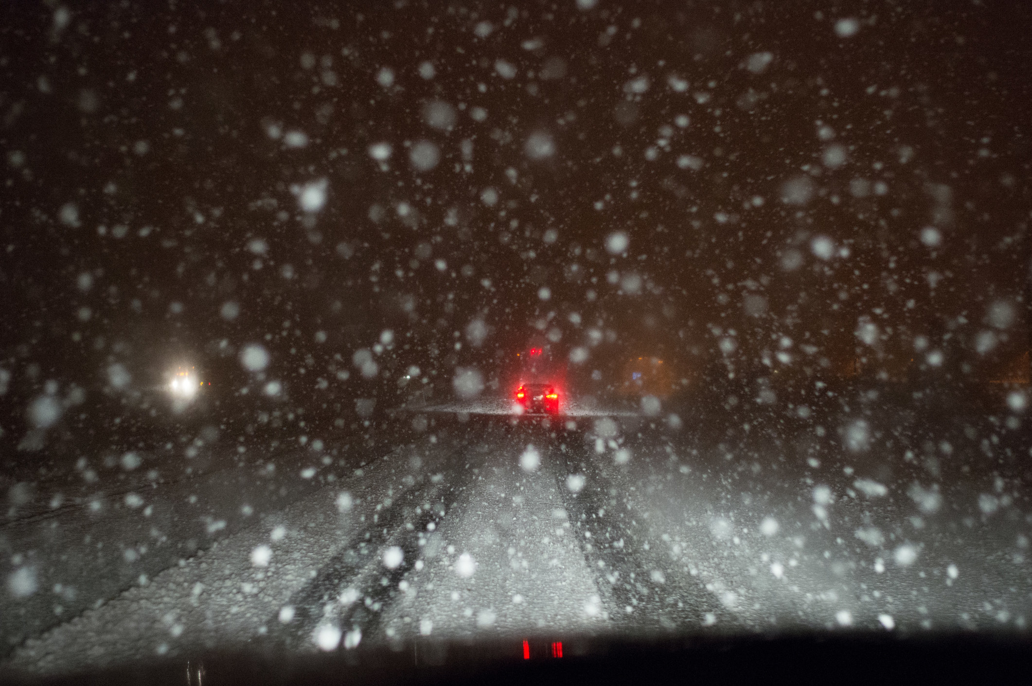 On a dark, snowy night, a pair of red brake-lights glow