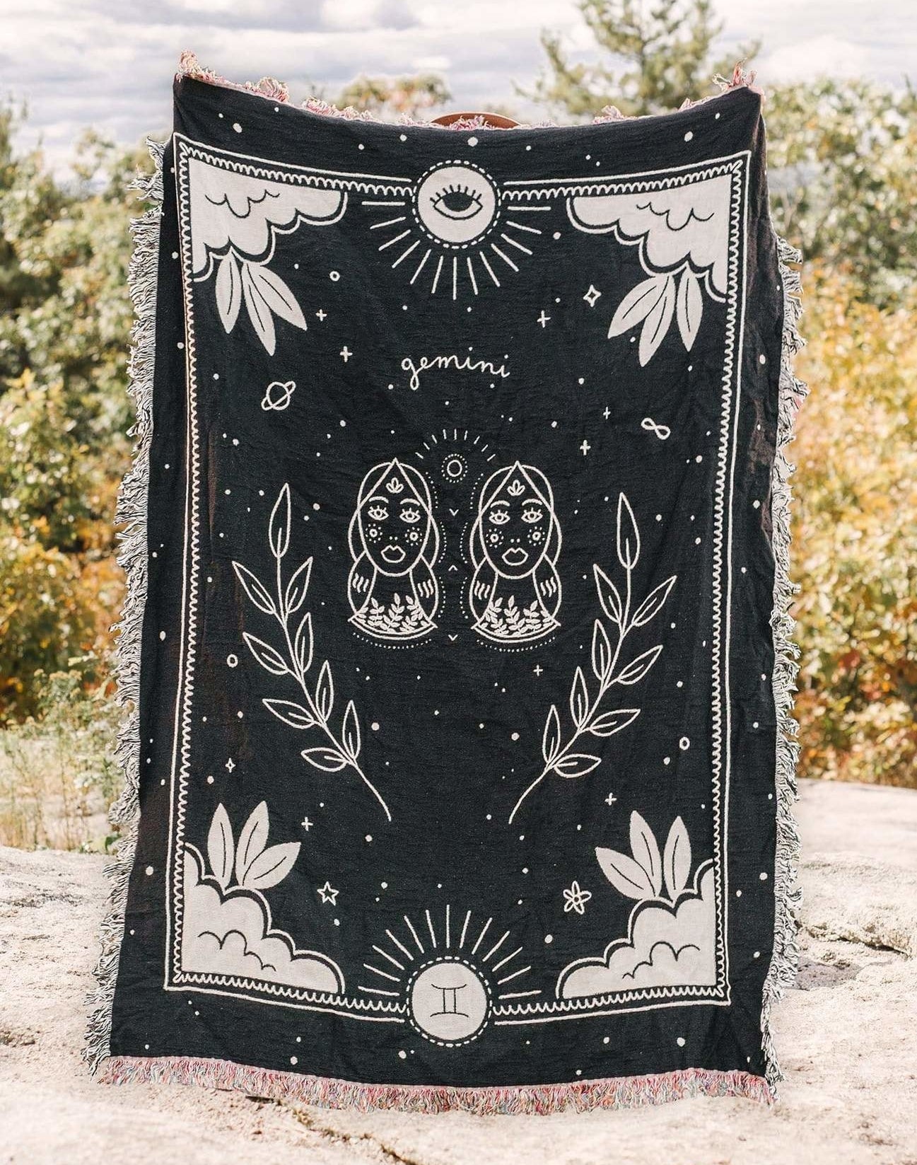 A black throw blanket with fringe throughout the edges and a celestial zodiac design on the front for Gemini