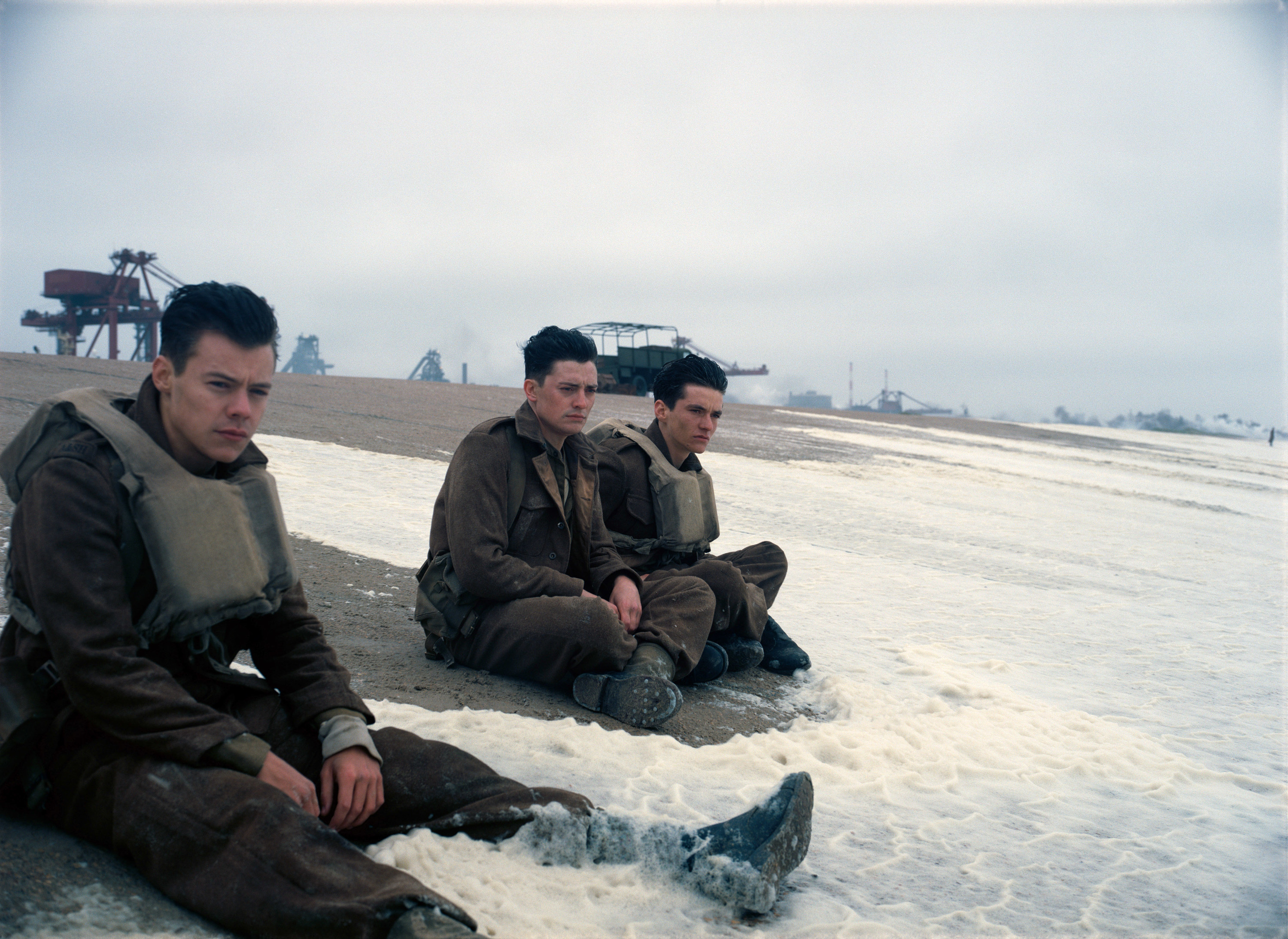 Harry Stiles, Aneurin Barnard, and Fionn Whitehead sit on a beach toghether in the waves