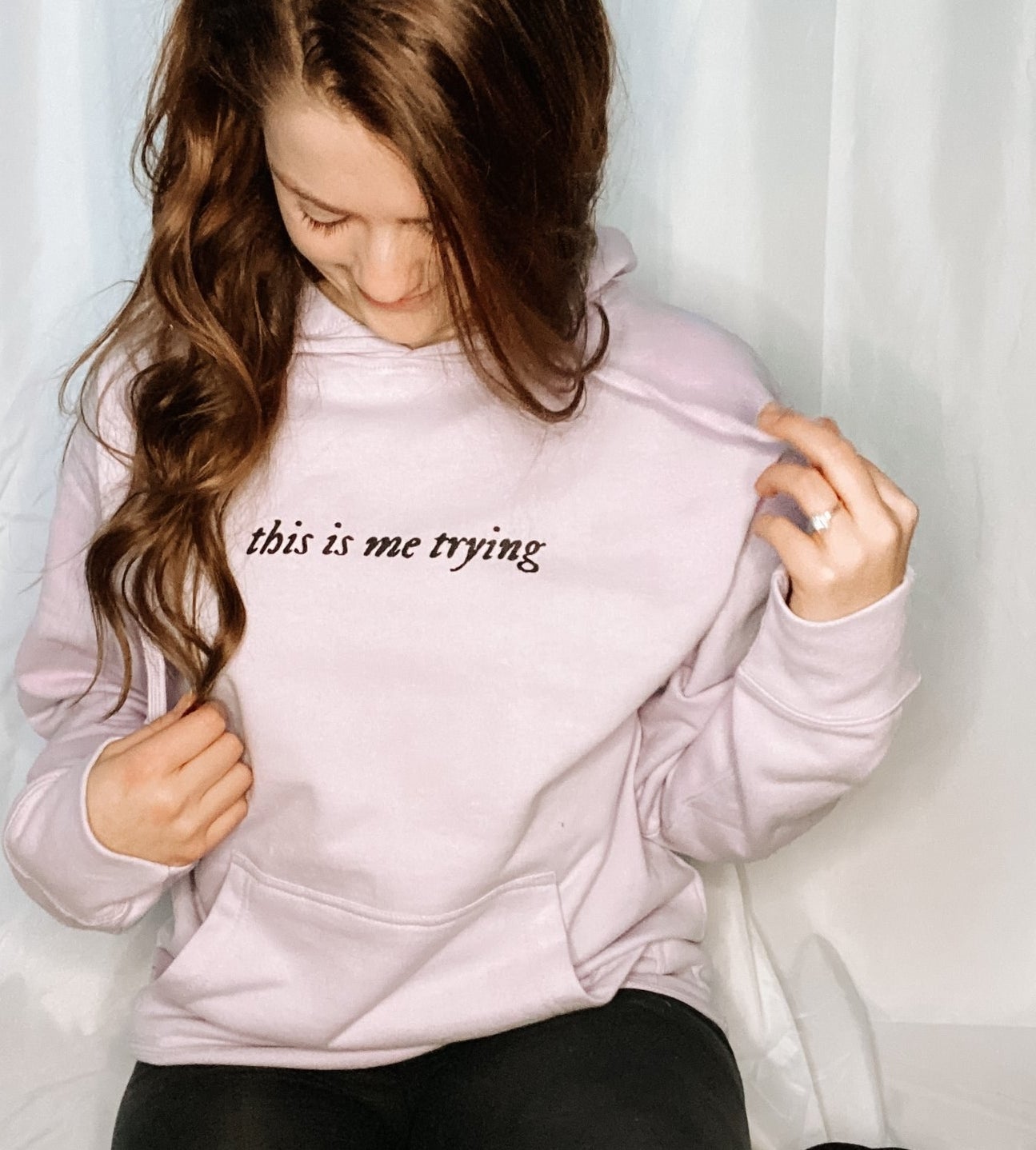 Model is wearing a light pink hoodie with the words &quot;This is me trying&quot; written in black