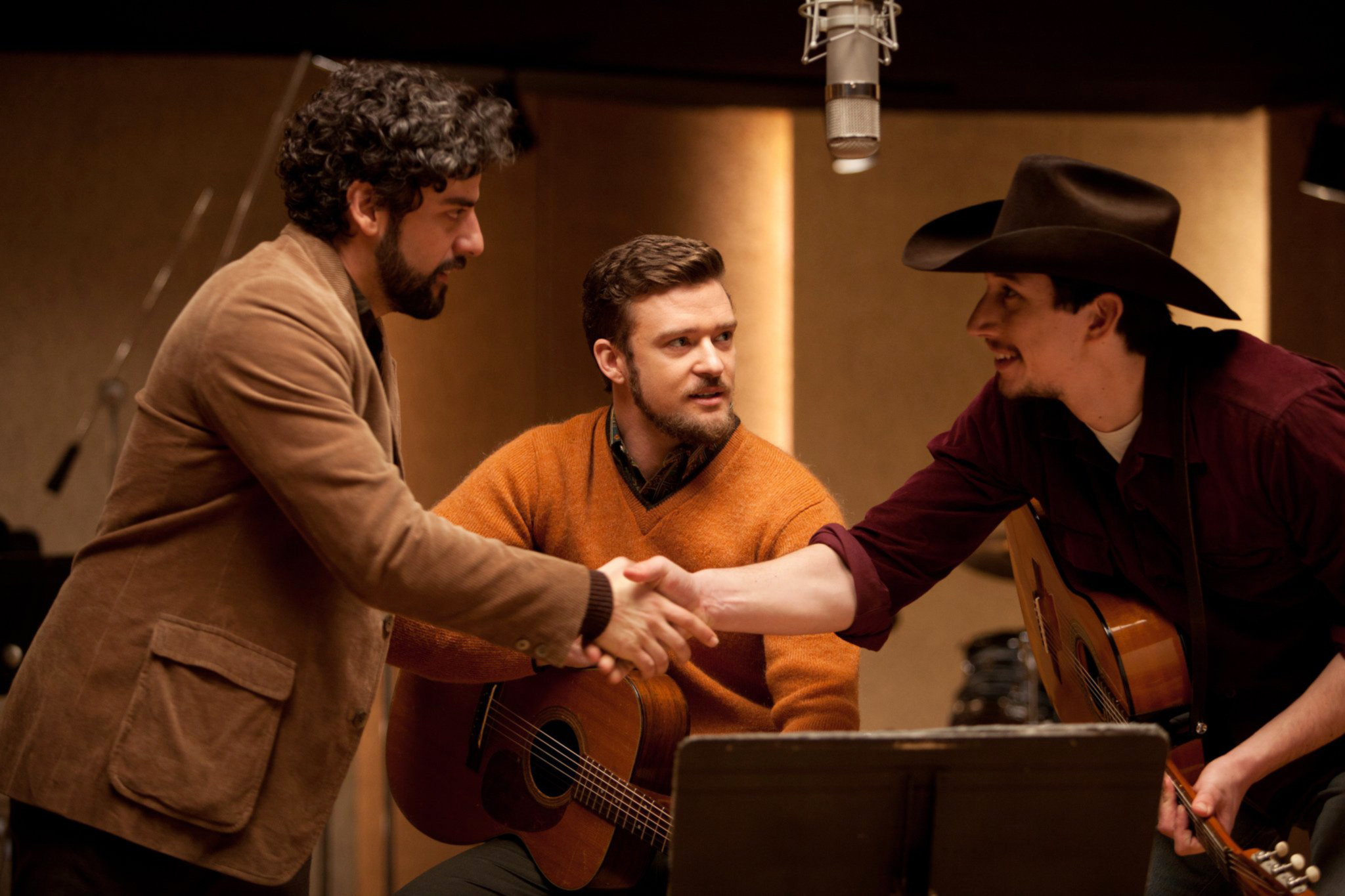 Justin Timberlake holds a guitar while Oscar Isaac and Adam Driver shake hands in front of him