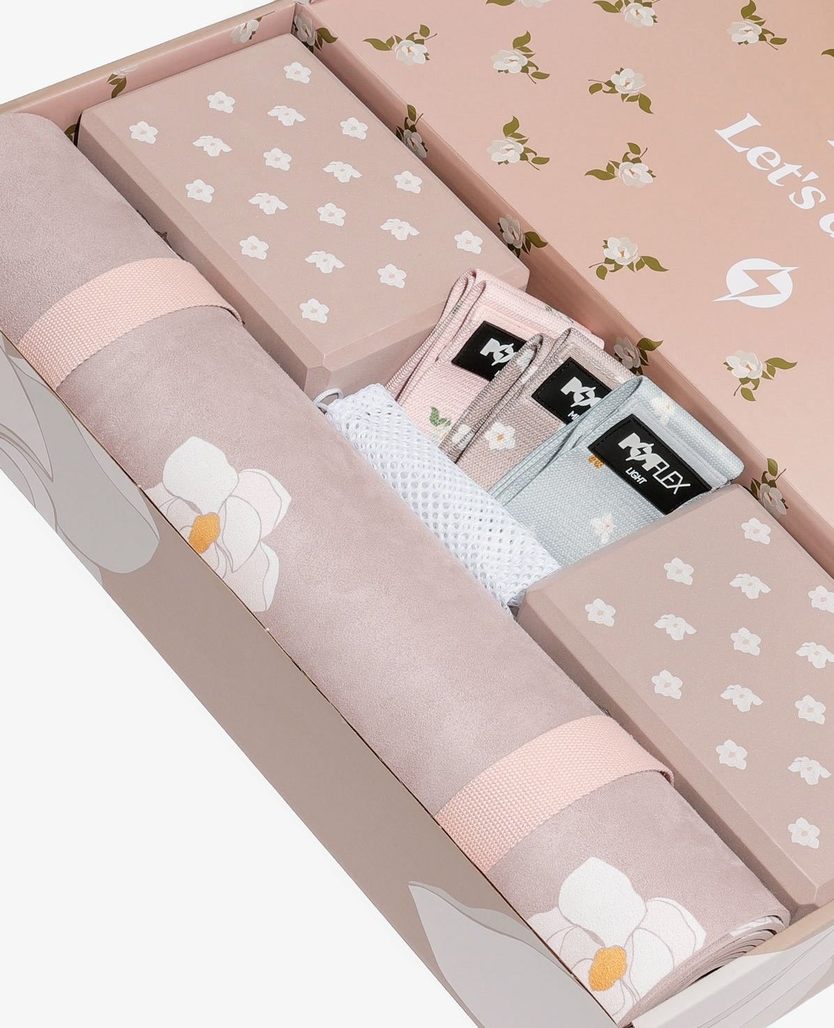 A pale pink box with a yoga mat, two yoga blocks, three bands, and a mesh bag, that all have magnolia flower graphics throughout