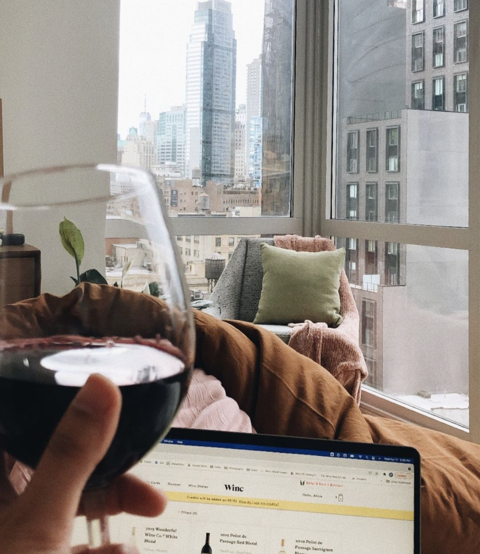 A person holding a glass of red wine as they scroll down Winc&#x27;s website