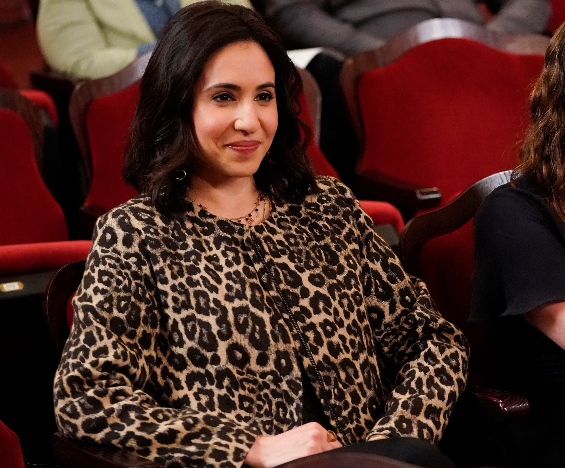 Valencia sitting in a theater seat and smiling while wearing a leopard-print top