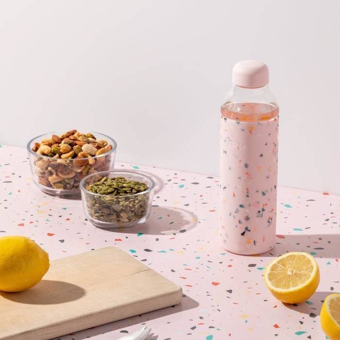 A pink glass water bottle with a terrazzo design throughout