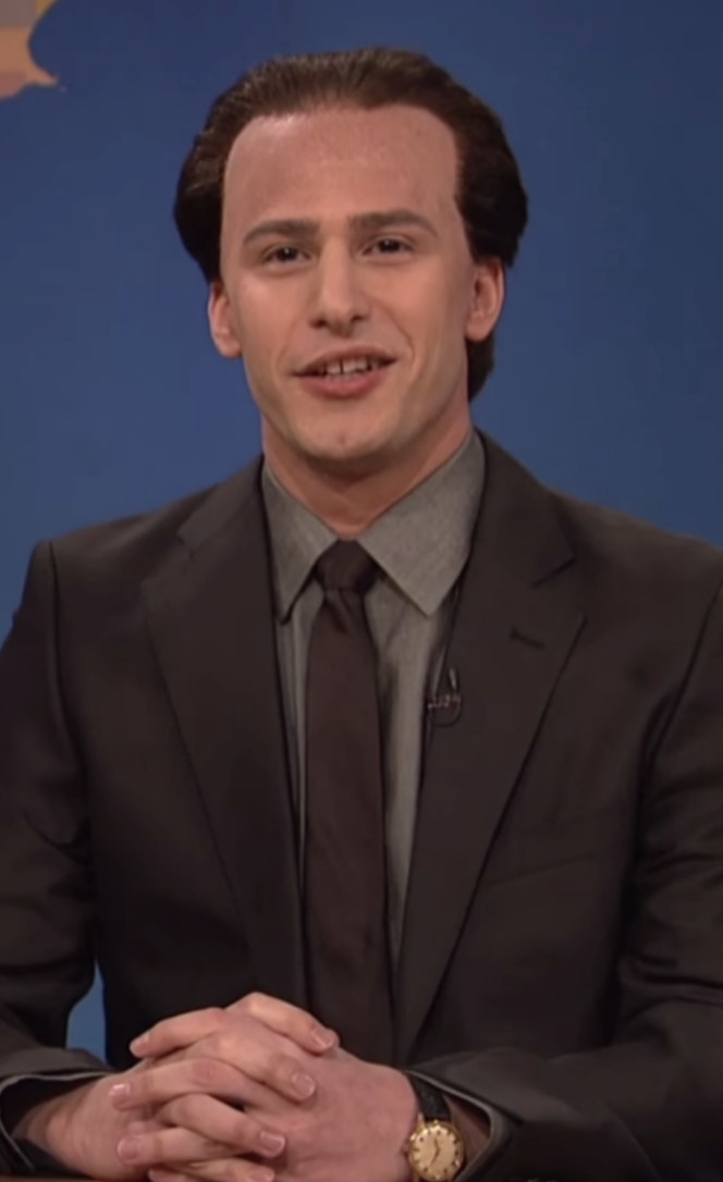 Samberg wearing a balding wig and a suit and tie