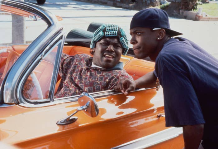 Tucker talks to Faizon Love, who's wearing curlers and sitting in the front seat of a car