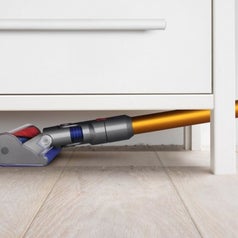 A cordless vacuum cleaning the floor under a dresser