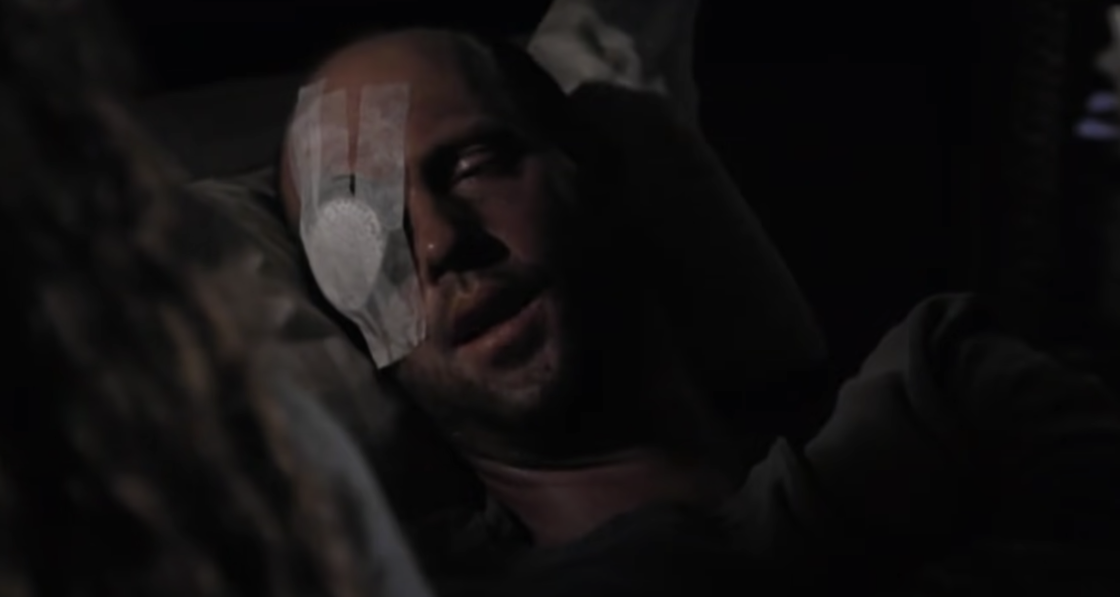 A visibly ill man with a bandaged eye lies in bed