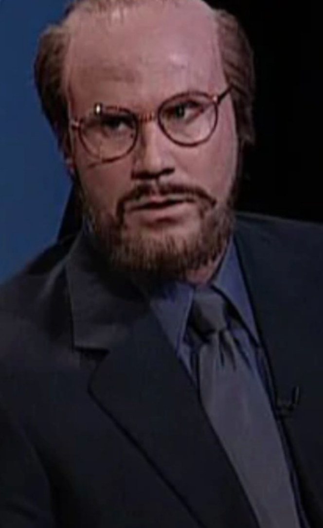 Ferrell wearing round glasses, suit and tie, beard, and balding wig