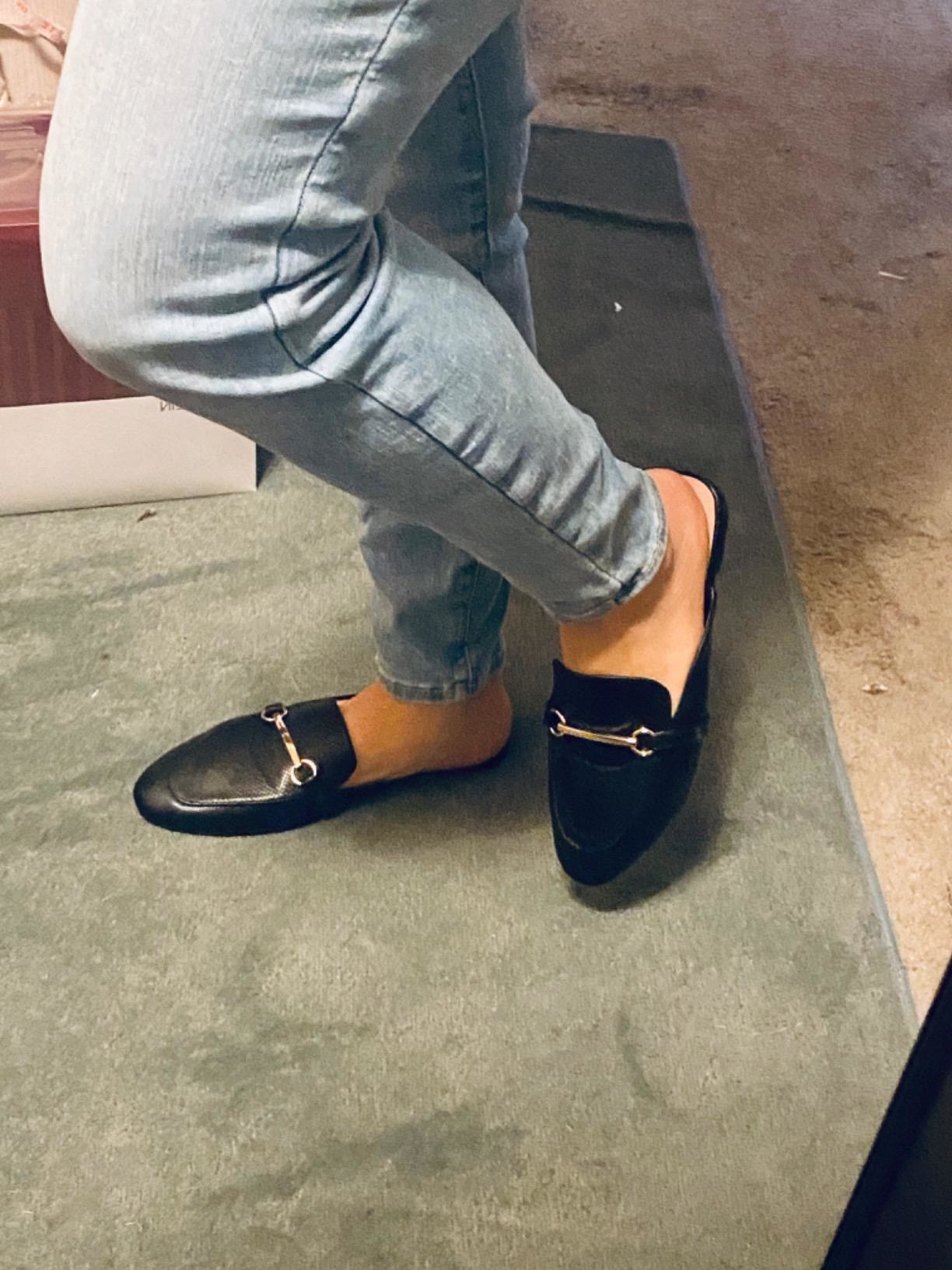 Reviewer wearing black mules with gold buckles