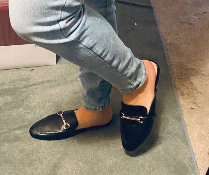 Reviewer wearing black mules with gold buckles