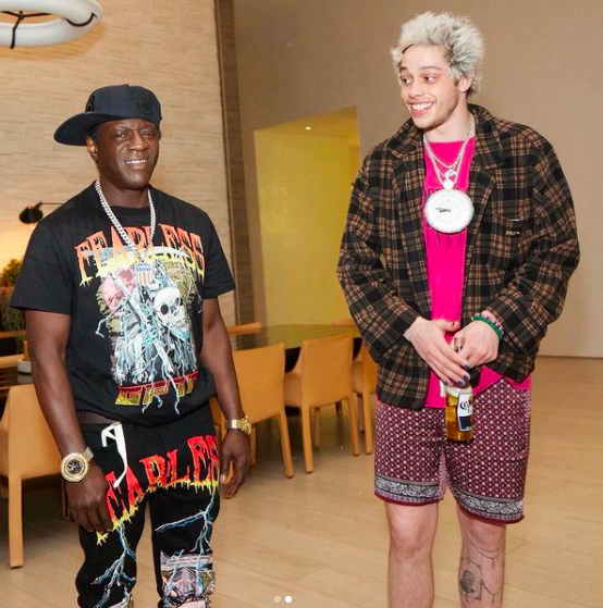 Flavor Flav standing next to Pete who&#x27;s wearing his clock around his neck and holding a Corona beer