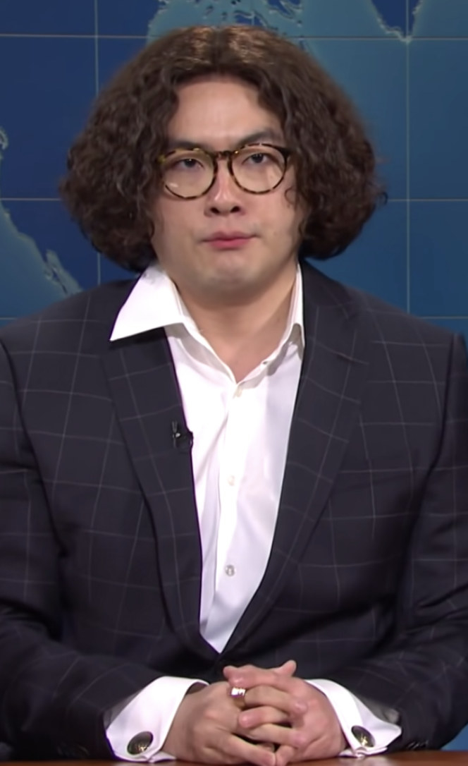 Yang wearing a short wig, round glasses, and a suit with a shirt underneath