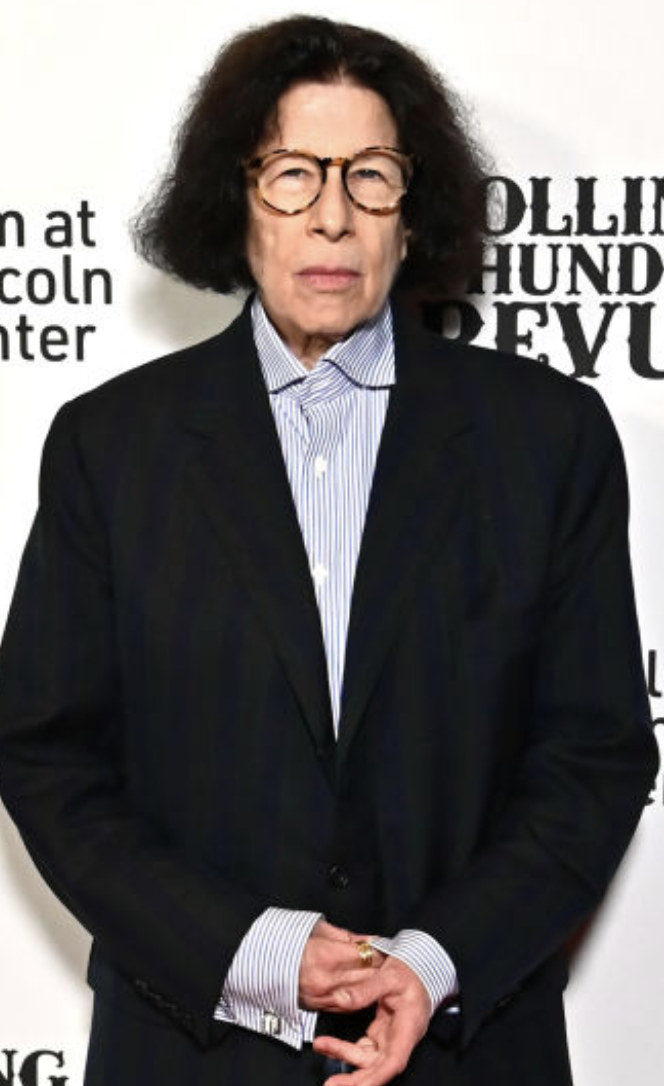 Lebowitz with short hair, round glasses, and a suit with a shirt underneath