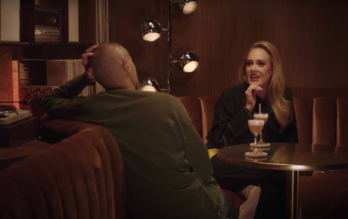 Adele puts her hand on her chin while speaking to Zane in a glam restaurant booth